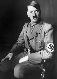 A white man with a mustache wears a military uniform with a Nazi emblem on his sleeve.