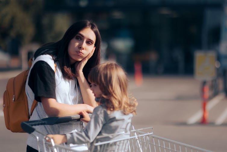 A mother with a grocery cart looks wiped