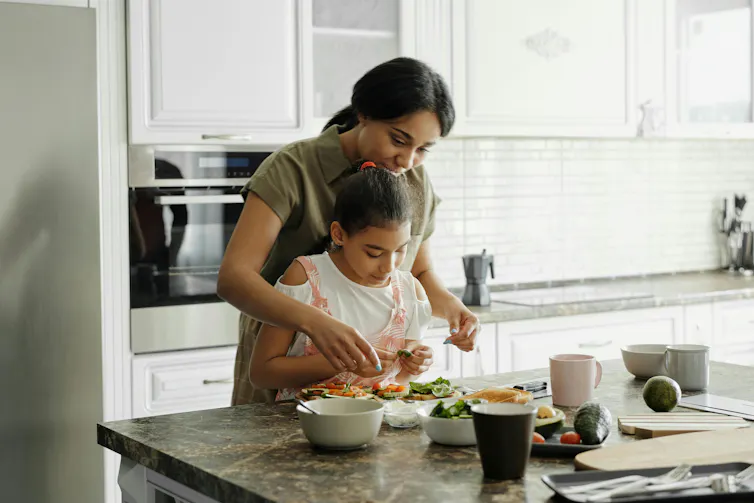 A mom standing behind daughter making food