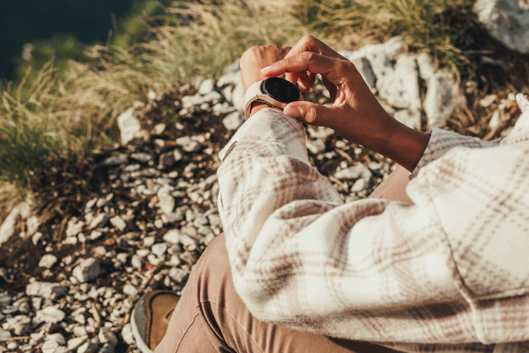 A woman's hands adjusting her smart watch while sitting outside.