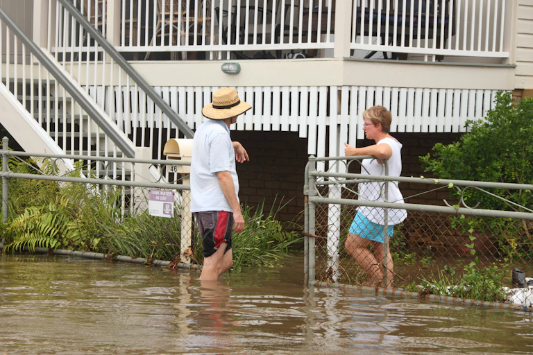 Man and woman leaning on fence, standing in flood water