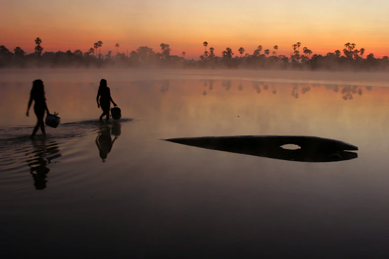 two indigenous women wade in water in Brazil