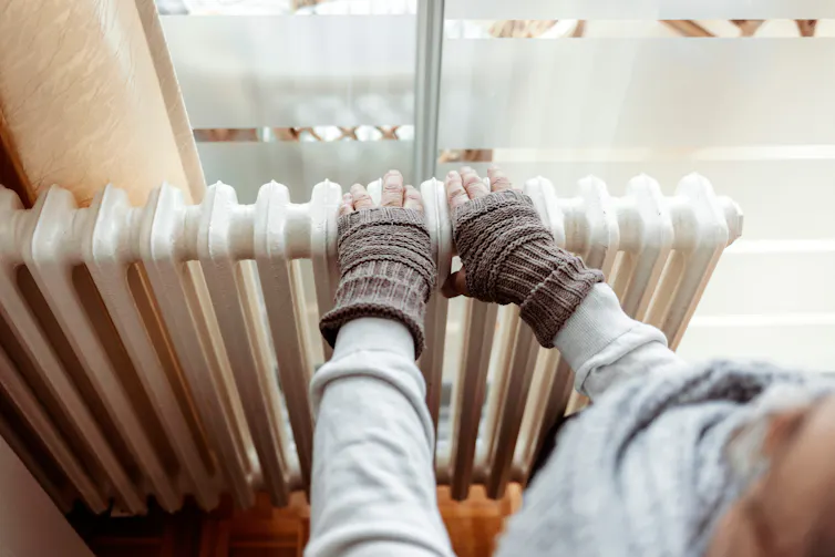 A person puts their gloved hands on a radiator to warm up