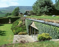 Underground house within green land, covered in grass and plants, windows at the side