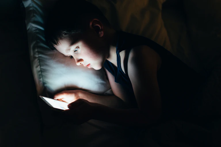 A young boy looks at a smartphone in the dark