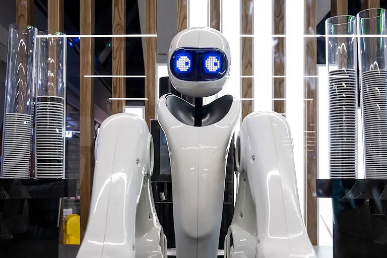 A white robot at a coffee shop with blue digital eyes to one side, looking shady.