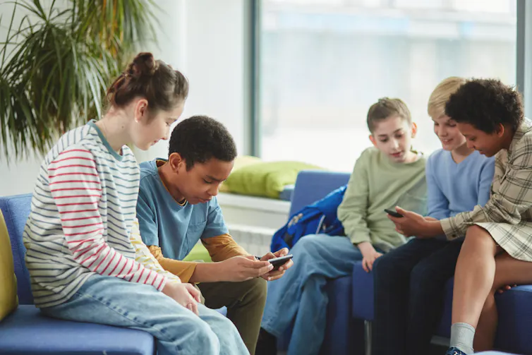 A group of children sit and look at smartphones