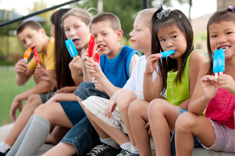 Children sat in a line eating ice lollies