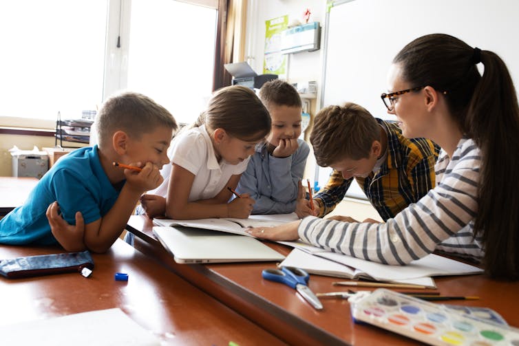Crianças e professora olhando para o trabalho escolar