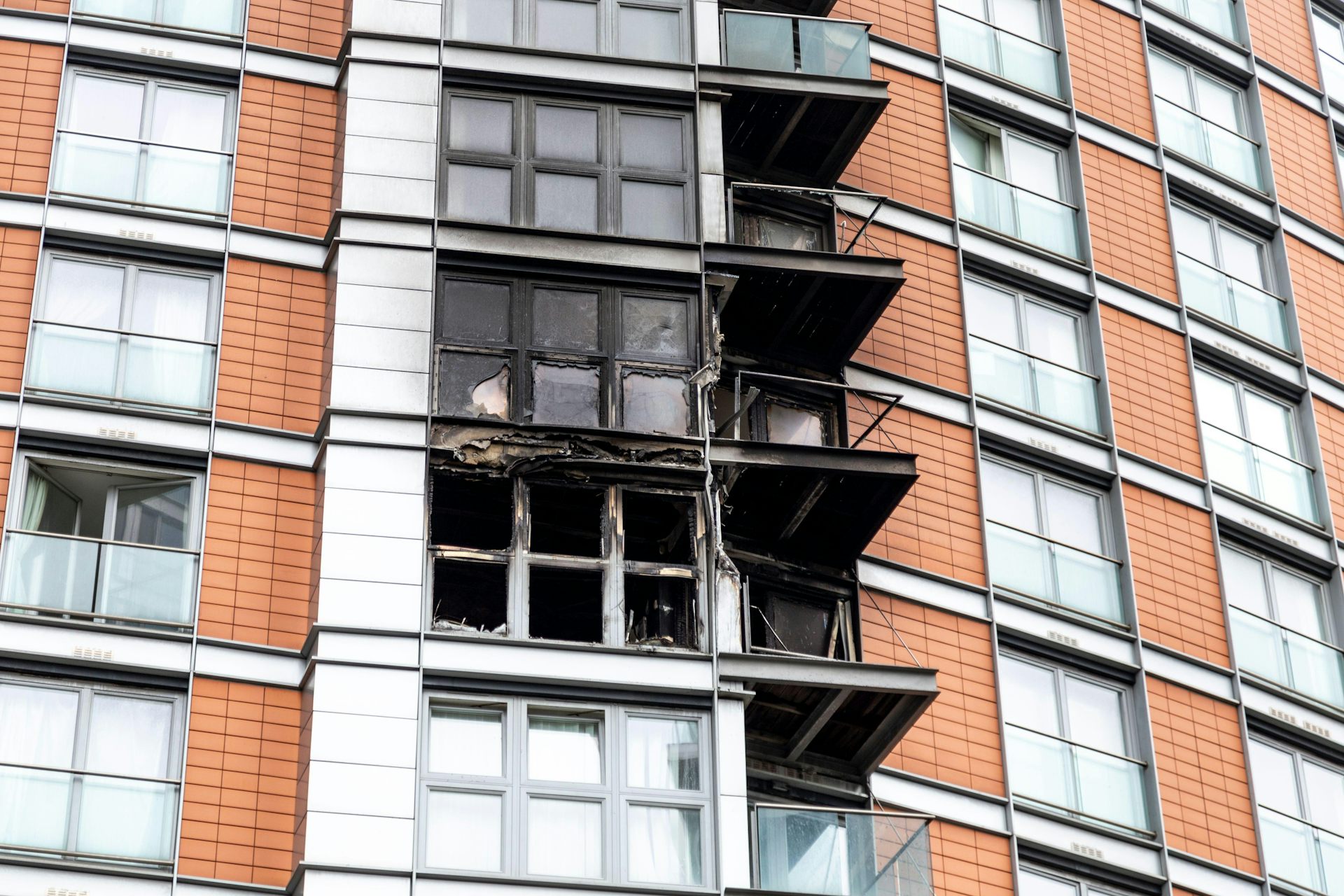 Três sacadas queimadas na lateral de um prédio revestido.