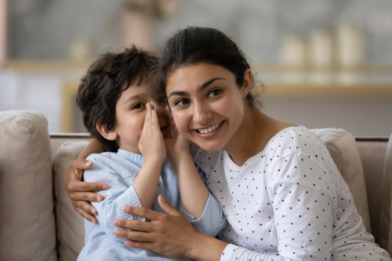 Small boy whispering in mother's ear