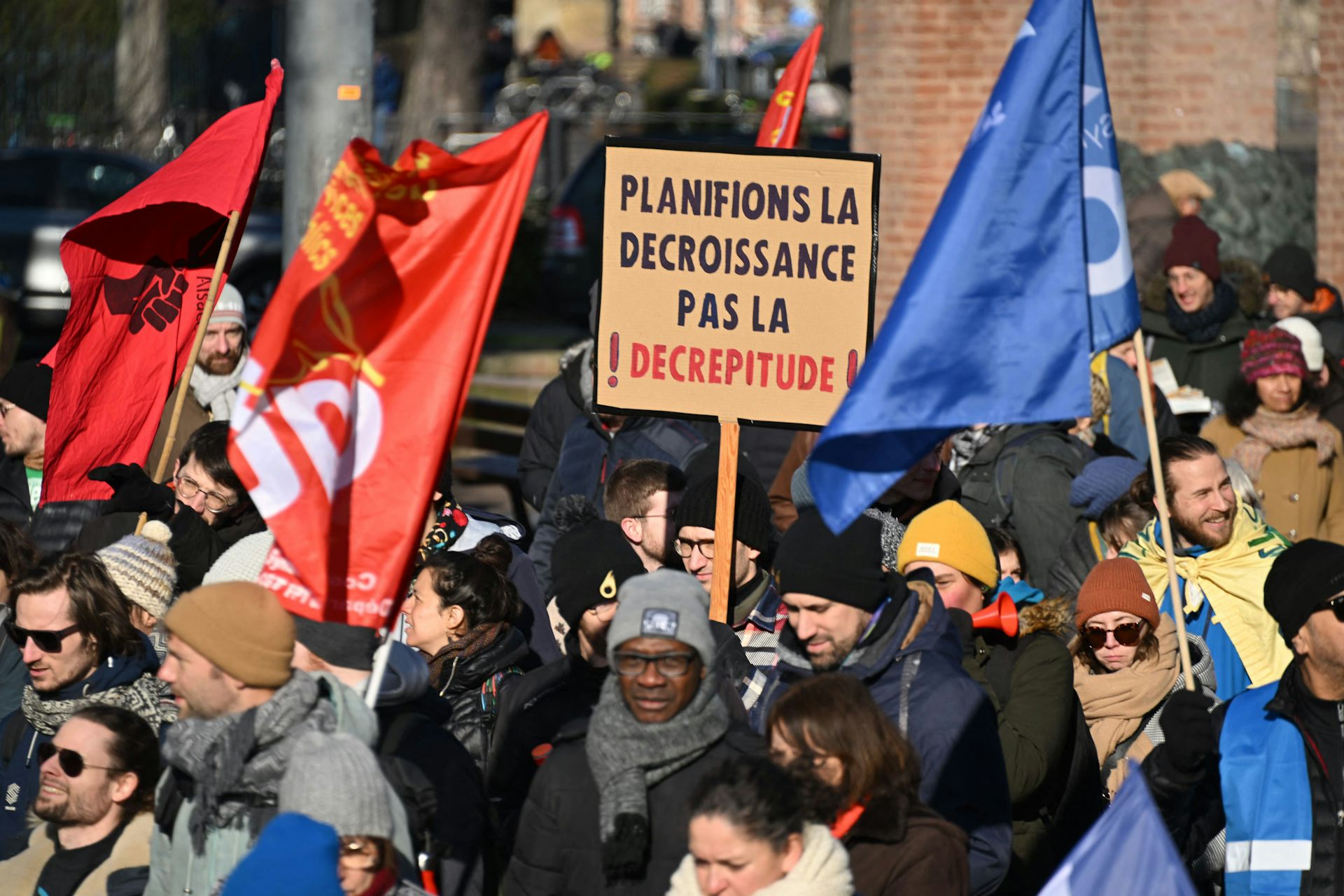 A person at a demonstration holds a sign in French that reads "Let's plan for degrowth, not decrepitude".