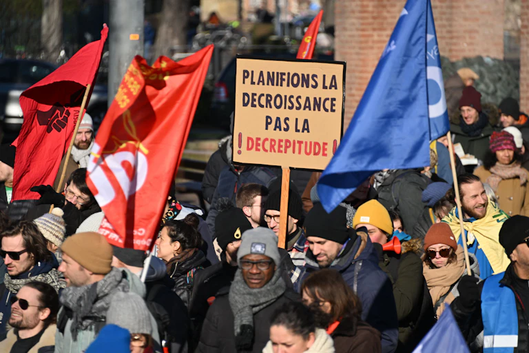 A person at a demonstration holds a sign in French that reads "Let's plan for degrowth, not decrepitude".