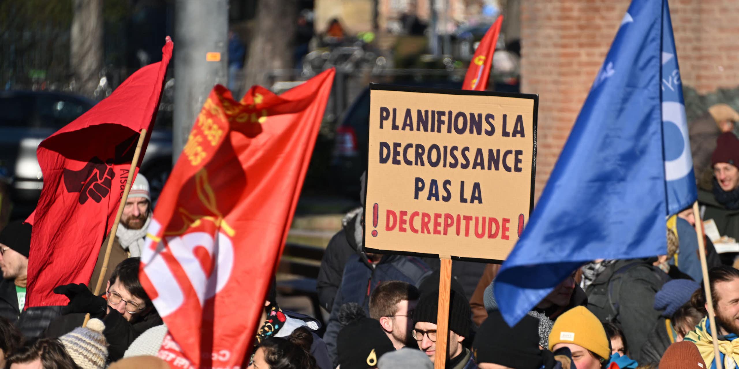 A person at a demonstration holds a sign in French that reads "Let's plan for degrowth, not decrepitude".