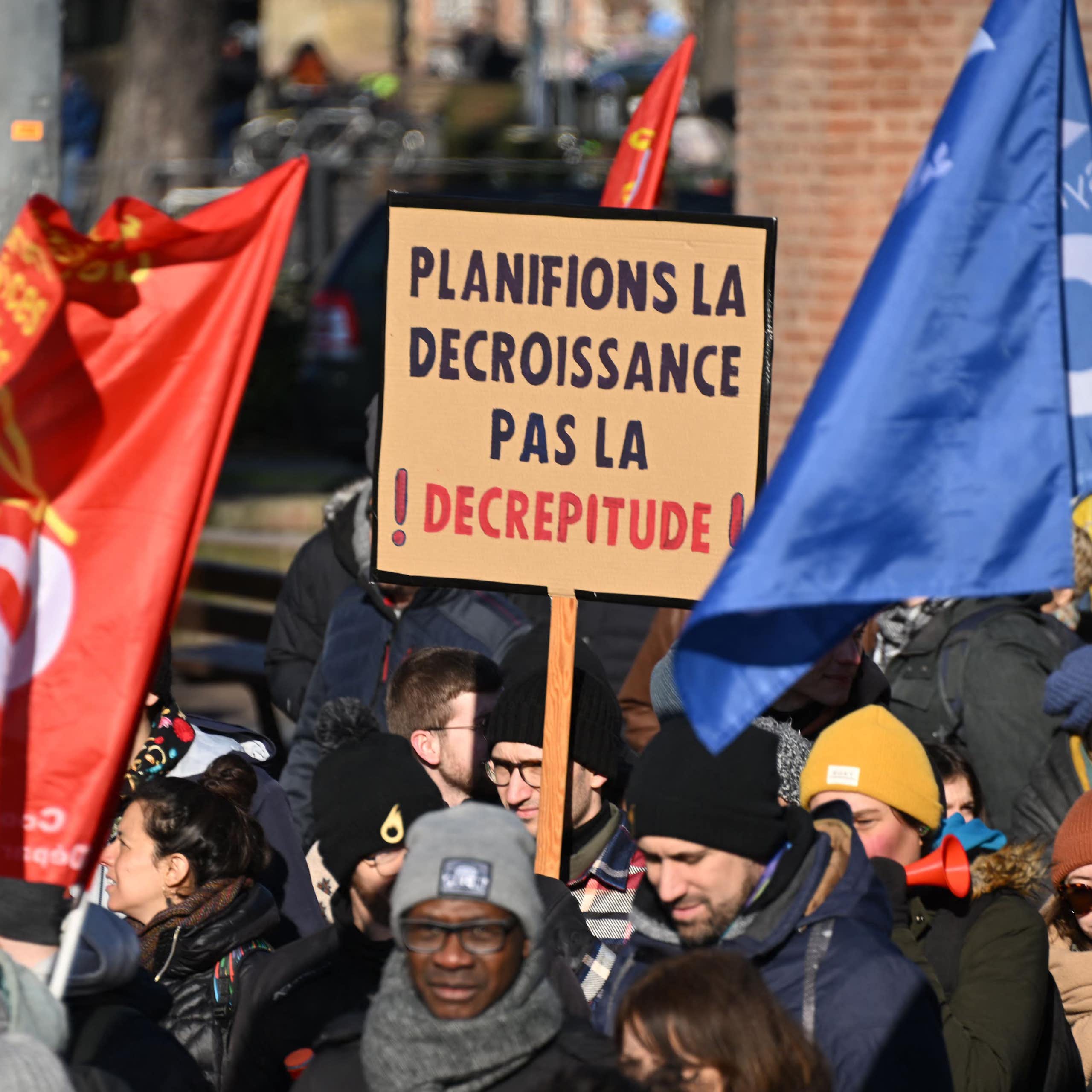A person at a demonstration holds a sign in French that reads "Let's plan for degrowth, not decrepitude".