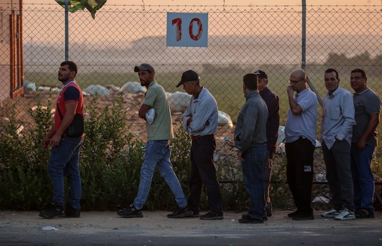 Palestinian workers queuing in a line in front of a fence.