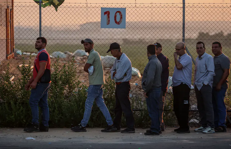 Palestinian workers queuing in a line in front of a fence.