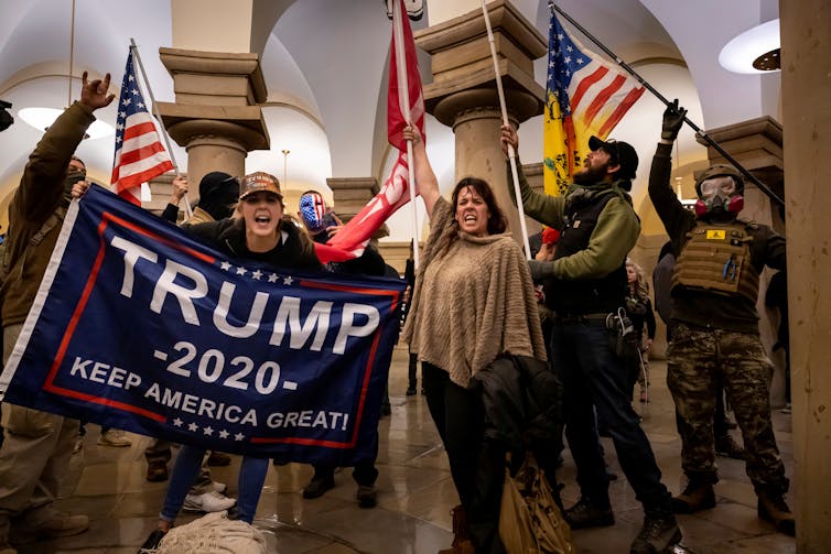 Several people shouting slogans, while holding American flags and a banners with with the words, 'Trump 2020, Keep America Great.'
