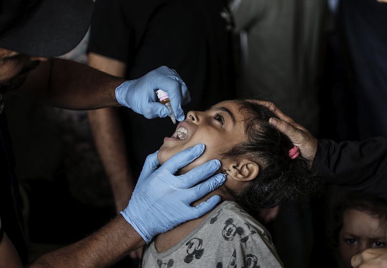A nurse administers polio vaccine drops to a Palestinian child.