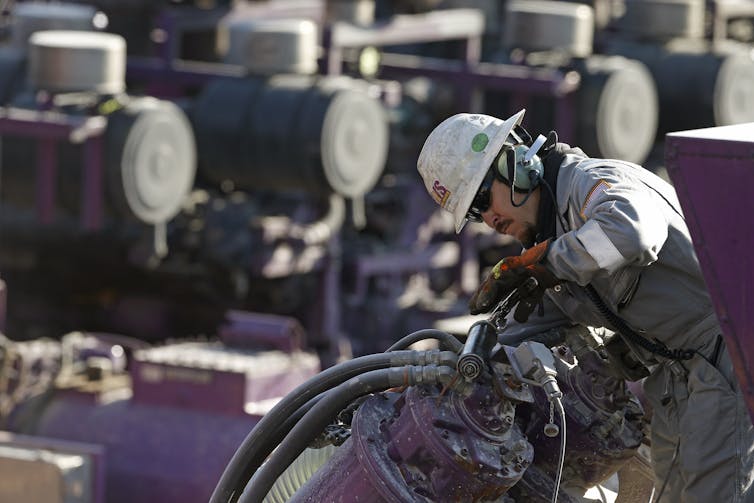 A man in a hardhat and coveralls works on machinery.