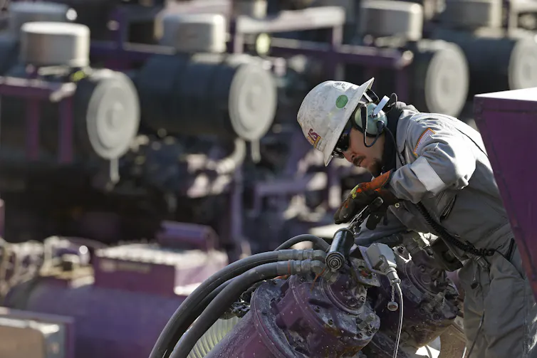 A man in a hardhat and coveralls works on machinery.