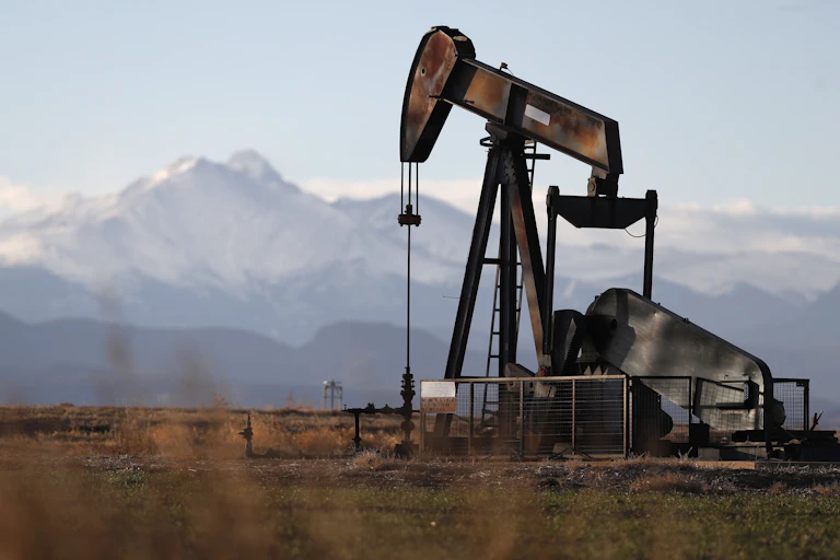 A pumpjack in Colorado with snow-covered mountains in the distance.
