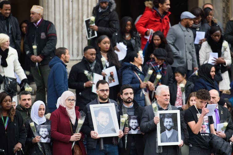 Pessoas saindo de uma igreja carregando fotos emolduradas das vítimas de Grenfell.