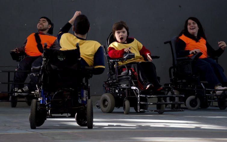 A man in a wheelchair with his back to the camera raises his fist while facing three of his teammates, who are also all in wheelchairs