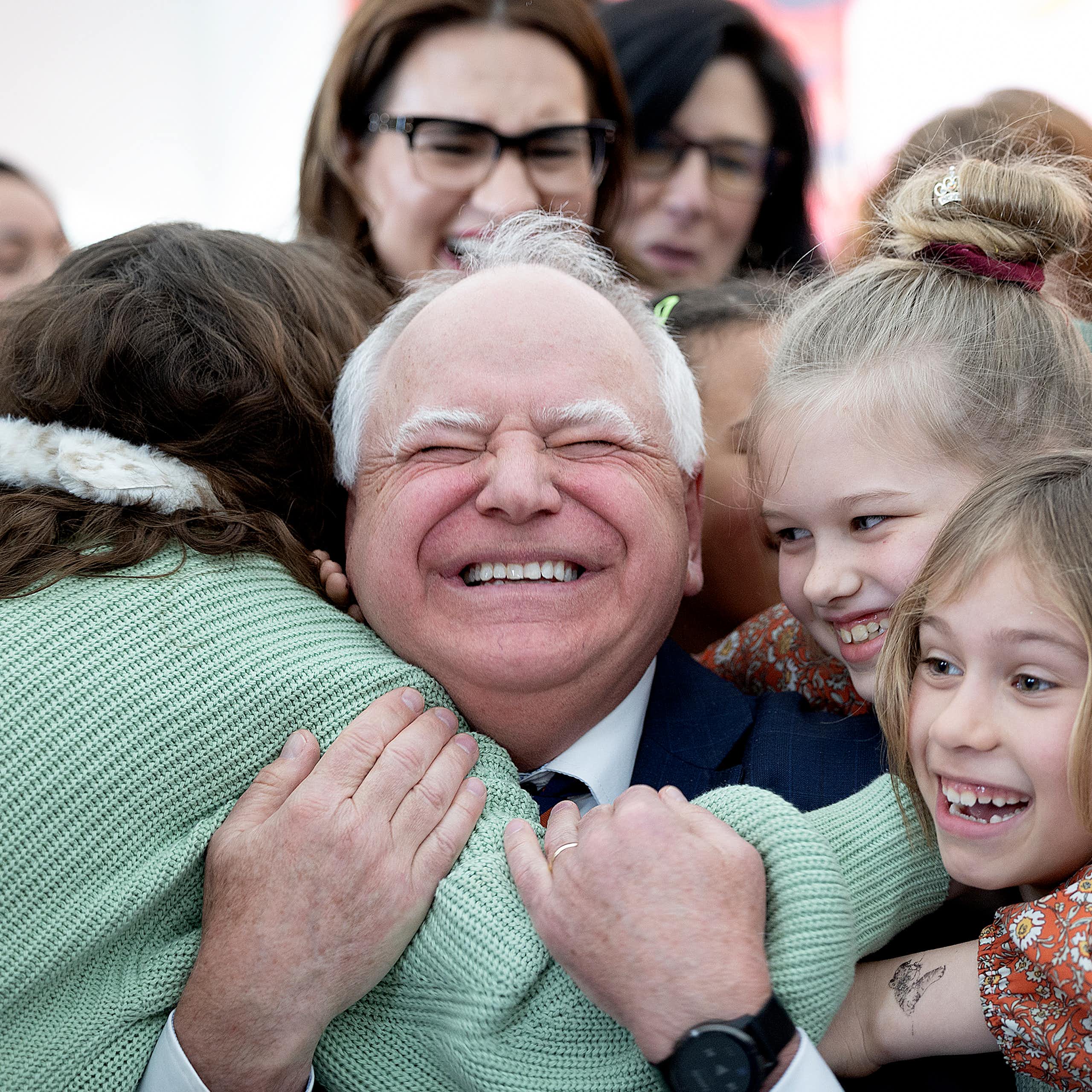 Gov. Tim Walz grins broadly and is thronged by excited children while adults look on.