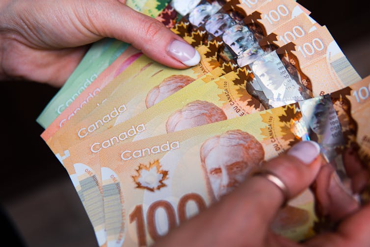 Closeup of a pair of hands fanning out a stack of Canadian dollar bills in varying amounts