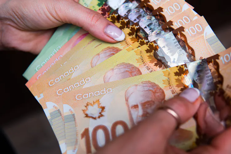 Closeup of a pair of hands fanning out a stack of Canadian dollar bills in varying amounts