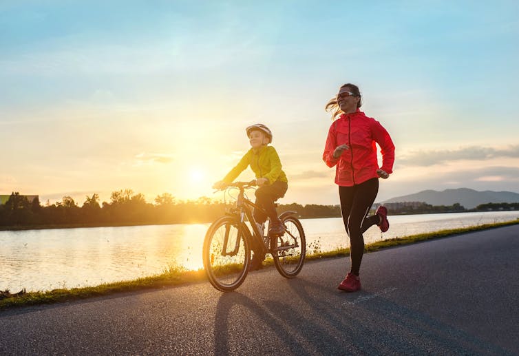 A woman running alongside a child riding a bike at sunset