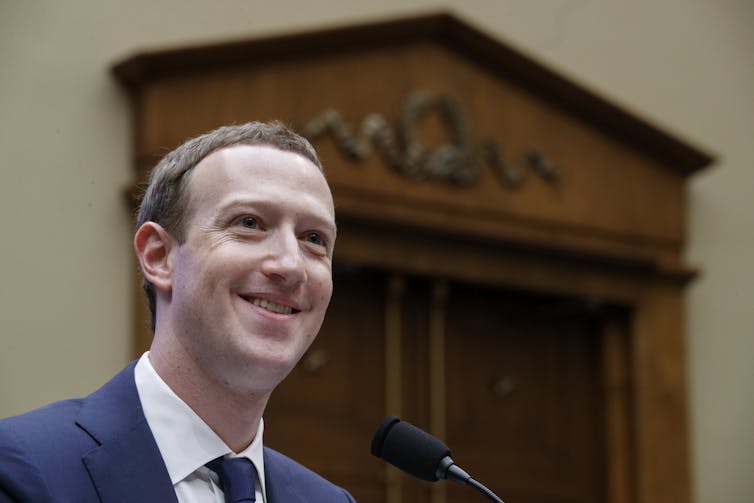 Man in suit smiling as he speaks into a microphone.