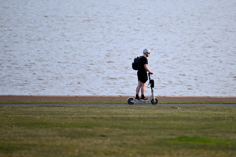 A man rides an e-scooter along a lakeside path