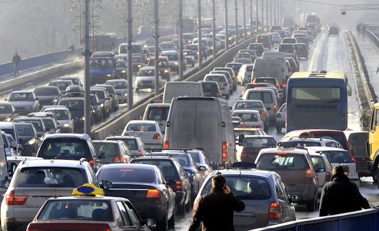 Pedestrians walk near a queue of traffic on a bridge.