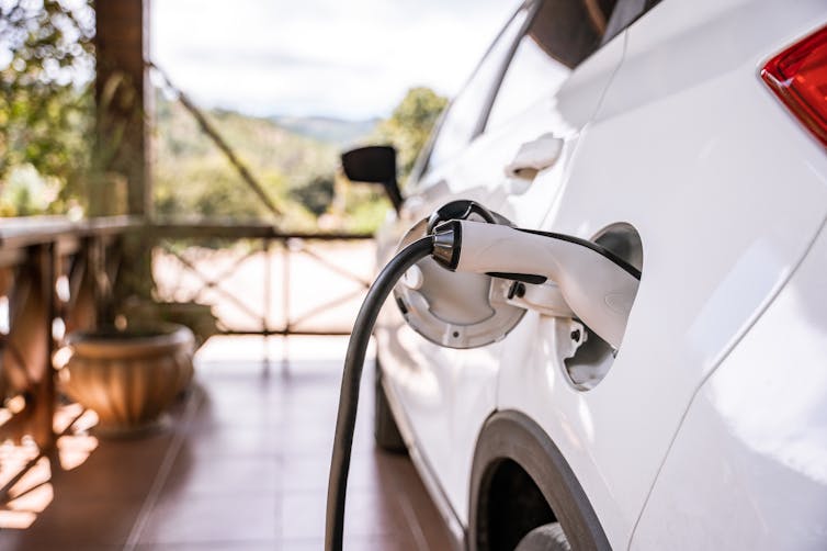 Charging an electric car at home, plugged in during a sunny day in an open-air carport