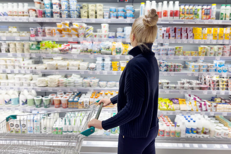 Une femme blonde pousse un chariot devant le rayon yaourt d'un grand magasin