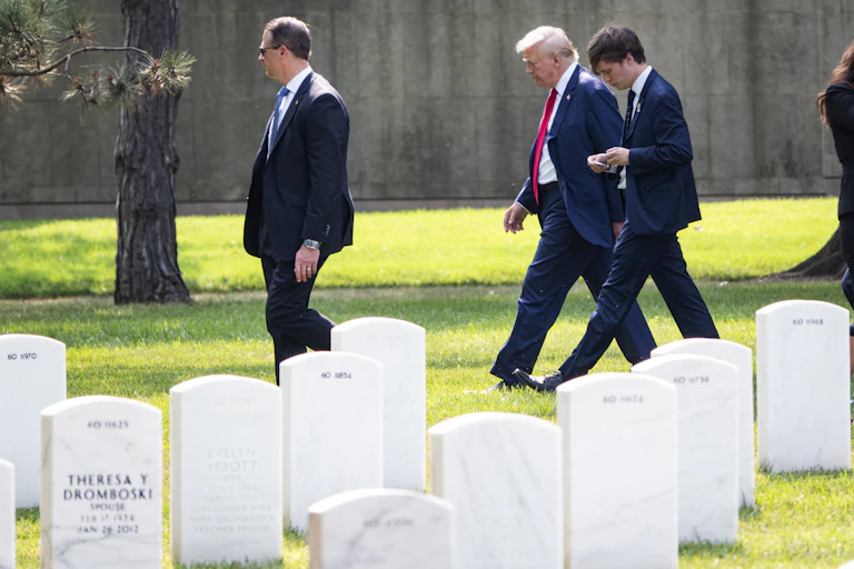 Three men in suits walk past rows of graves.