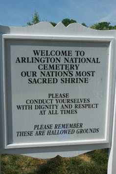 A sign reads 'Welcome to Arlington National Cemetery, our nation's most sacred shrine. Please conduct yourselves with dignity and respect at all times. Please remember these are hallowed grounds.'