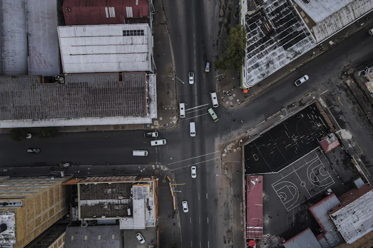 An aerial view of an urban area, minibus taxis at an intersection and sports pitch painted on tarmac among building tops.