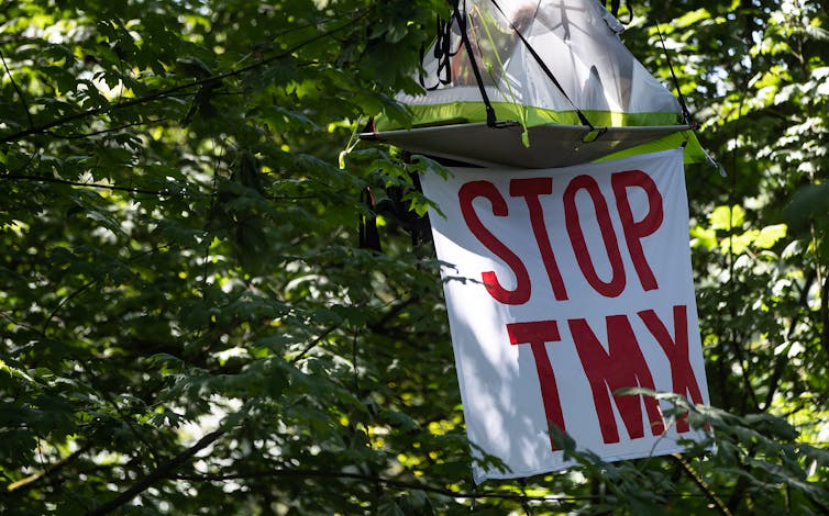 A tent-like structure suspended in trees with a sign saying stop TMX.