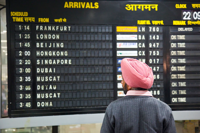 A man wearing a pink turban looks at an airport arrivals screen.