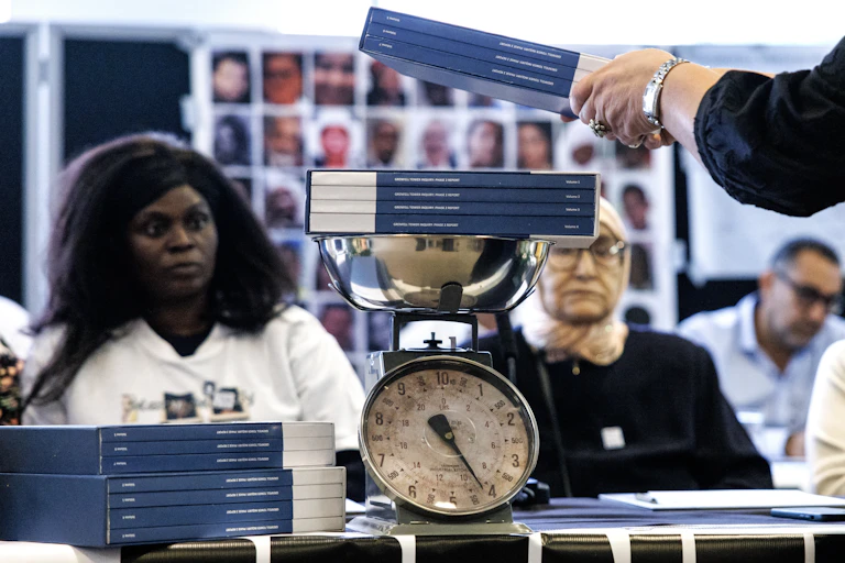 Volumes of the Grenfell inquiry report are placed on a weighing scale while two women look on.