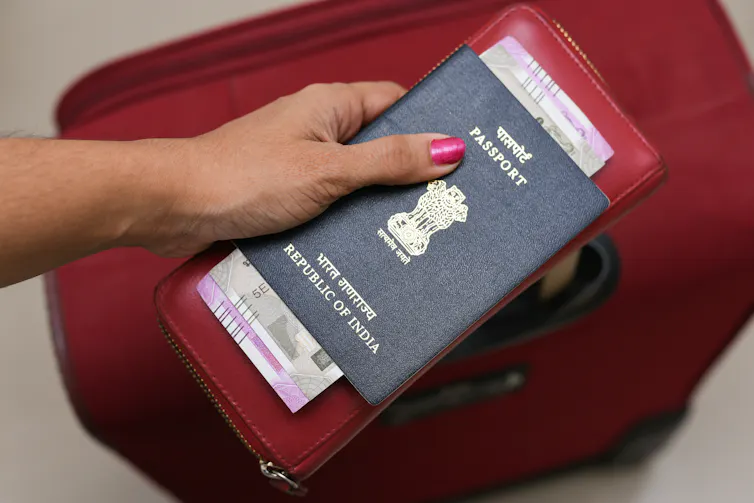 A female tourist holding her Indian passport, a currency note and a suitcase.