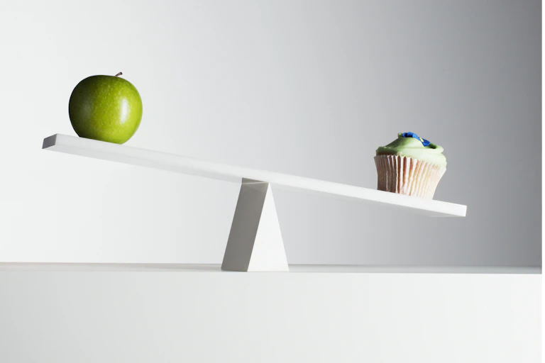 Balancing scale with green apple on the higher end and a cupcake on the lower end