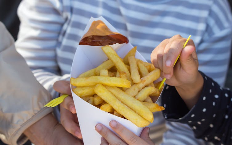 Three people holding a cone of french fries.