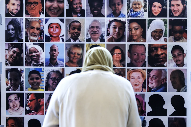 View from behind of a woman in a headscarf looking at a wall of photos of victims