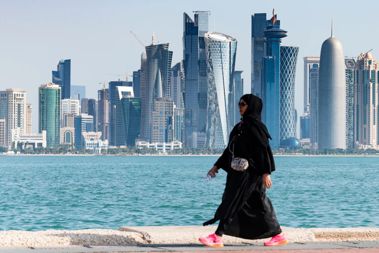 A woman walking along the waterfront with the Doha city skyline in the background.