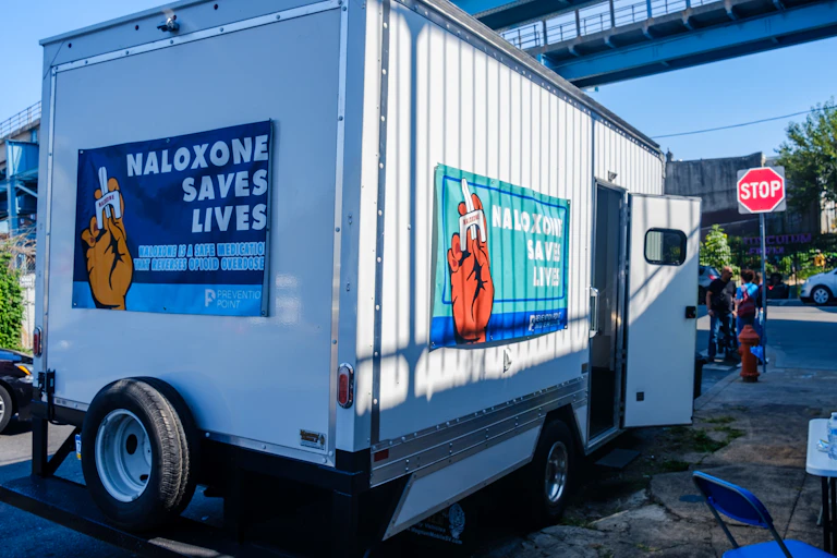 A large white van is parked on Philadelphia street and has signs that read 'Naloxone saves lives'