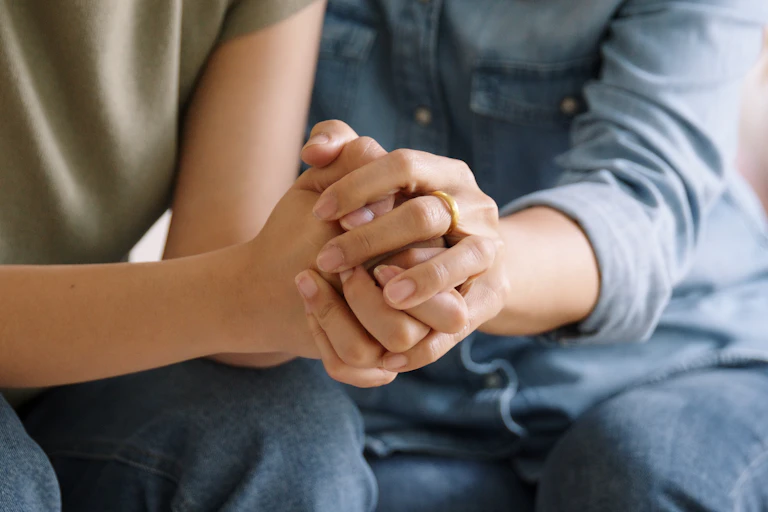 Close up of a woman grasping her daughter's hand in support while the two are seated side by side on a couch